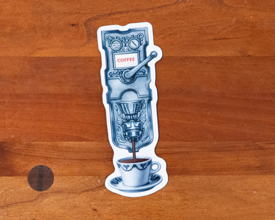 A die-cut sticker featuring a vintage coffee machine dispensing coffee into a cup, placed on a wooden tabletop.
