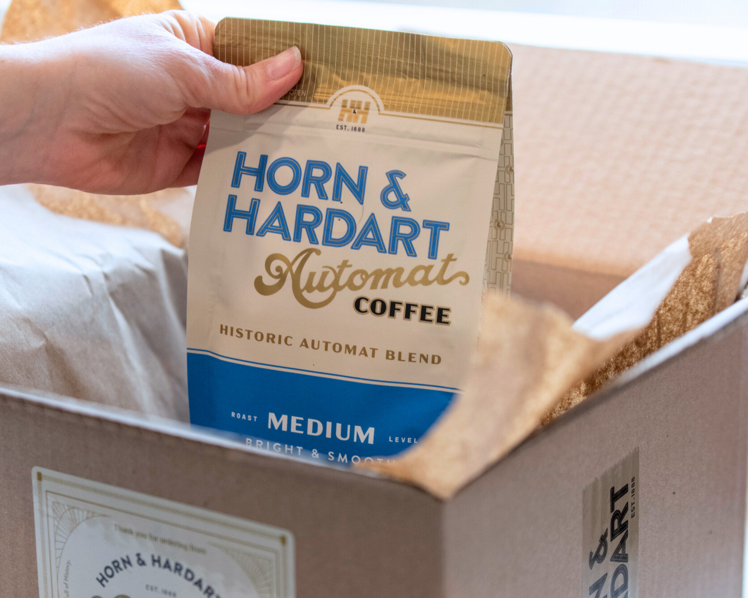 Hand pulling out a bag of medium roast Automat coffee from a box