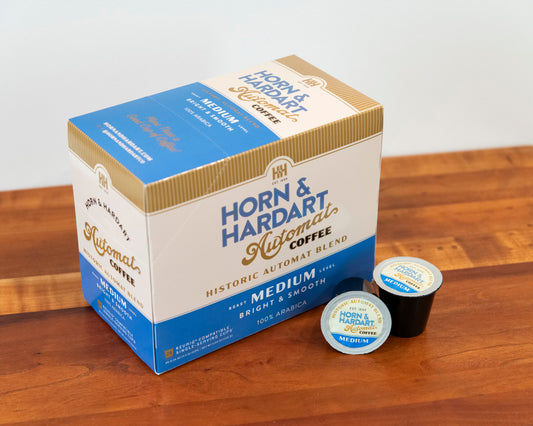 Horn & Hardart coffee box with two single-serve coffee pods on a wooden surface.