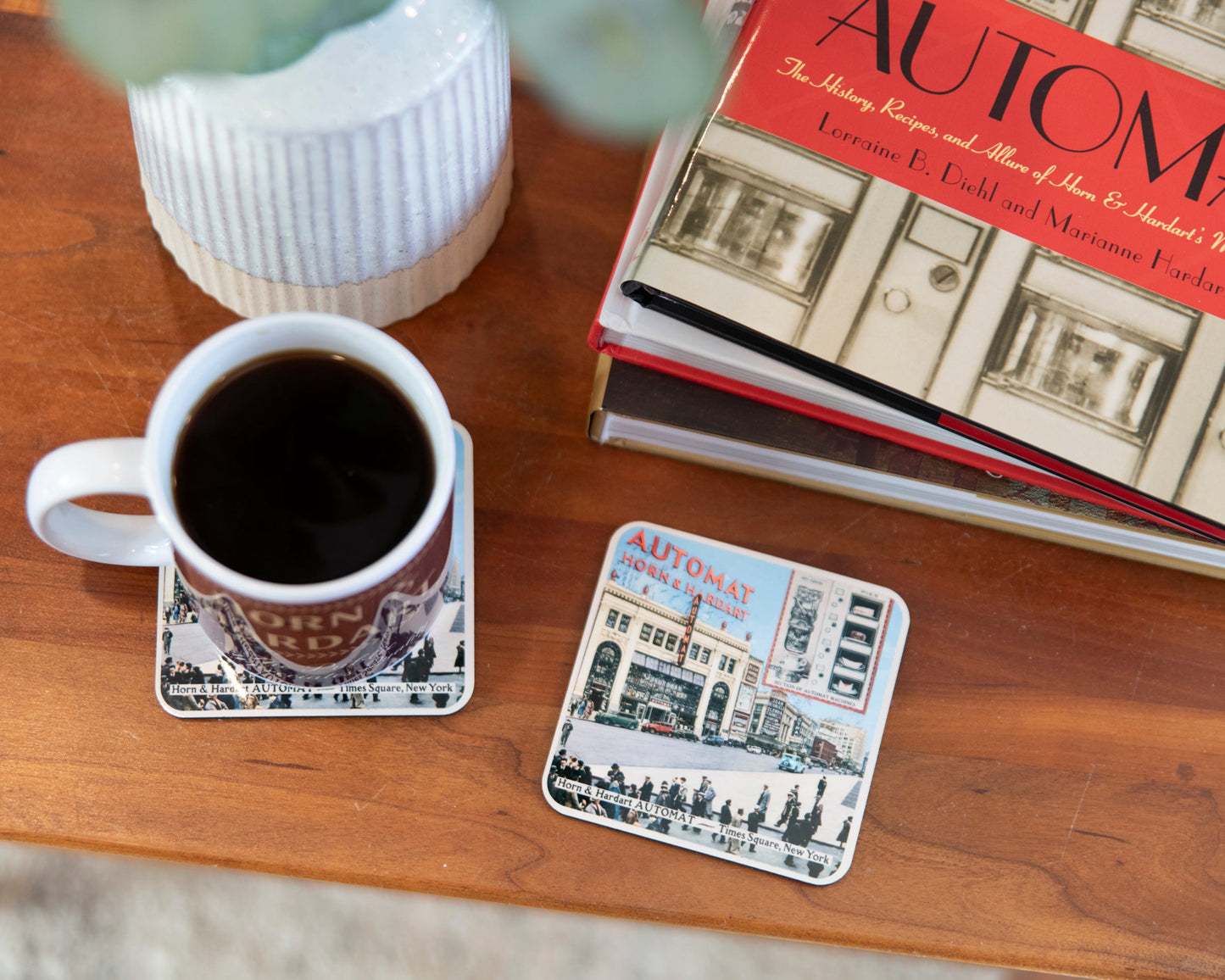 Cup of coffee on a coaster with a book titled 'Automat' on a wooden table.