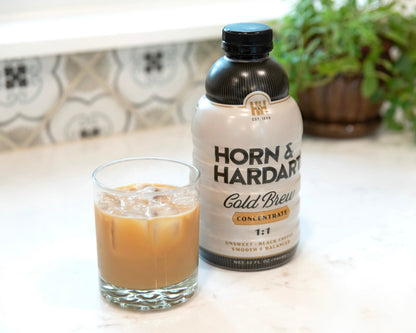 A bottle of Horn & Hardart Cold Brew Concentrate next to a glass of iced coffee on a light marble countertop with a blurred kitchen background.