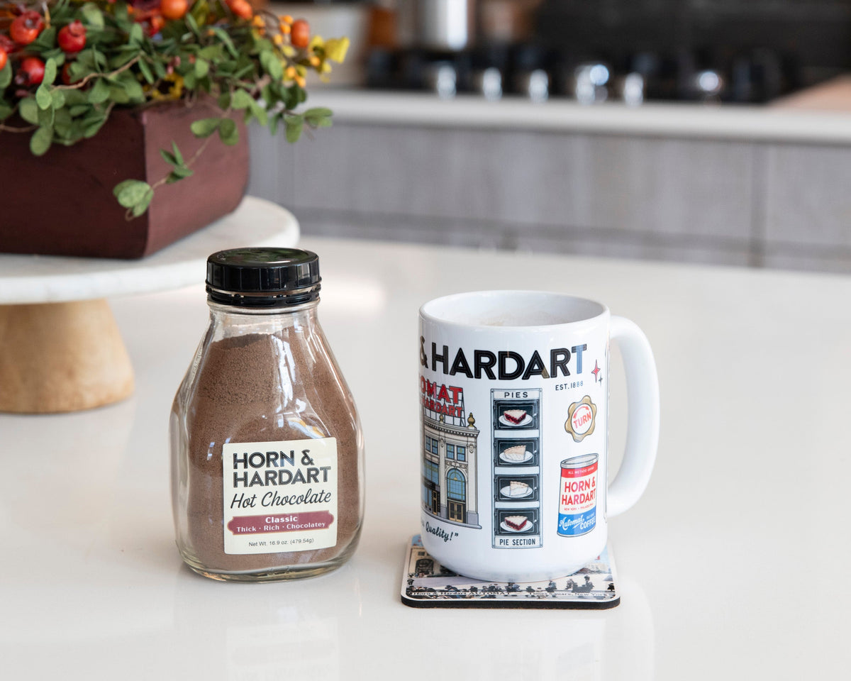 Hot chocolate sits next to a H&H memories mug in a warm kitchen.