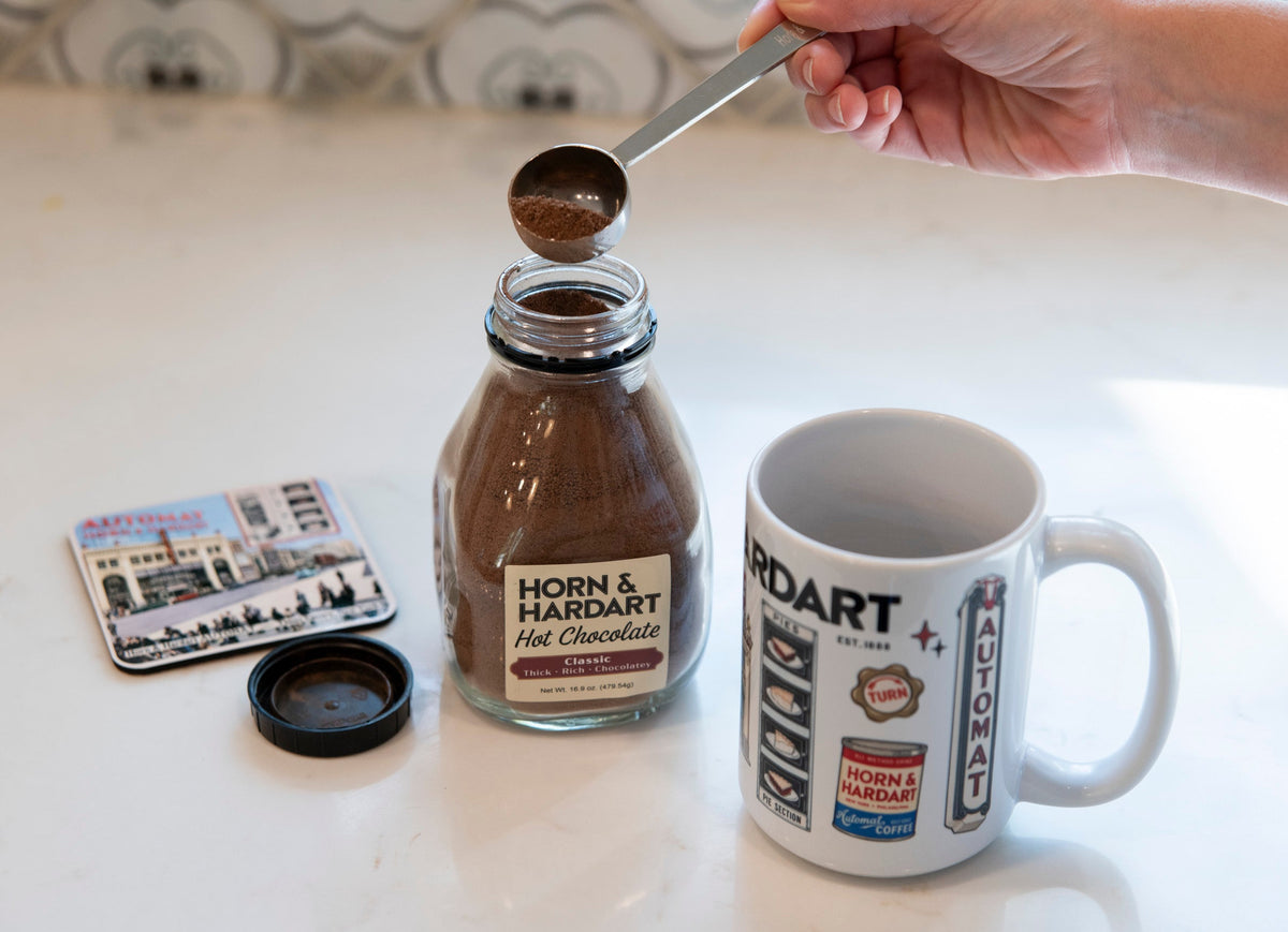 Hand scooping Horn & Hardart hot chocolate next to a mug and coaster