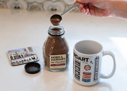 Hand scooping Horn & Hardart hot chocolate next to a mug and coaster