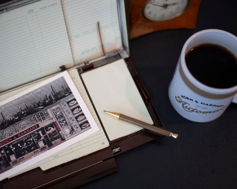 Open notebook with printed page, pen, and coffee cup on a dark surface