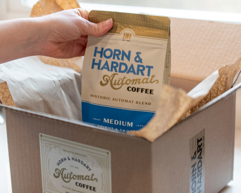 Horn & Hardart coffee package being held above a cardboard box with the brand's logo.