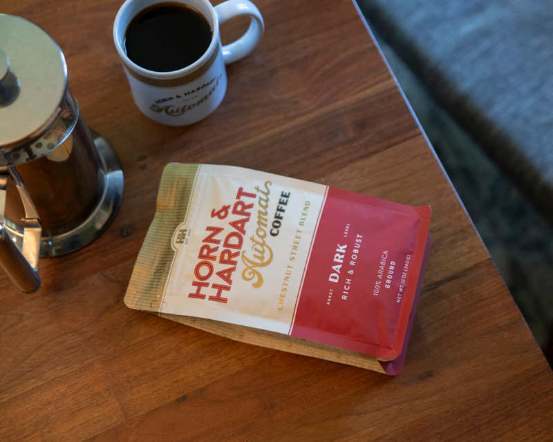 Horn & Hardart coffee package with a cup of coffee and French press on a wooden table.